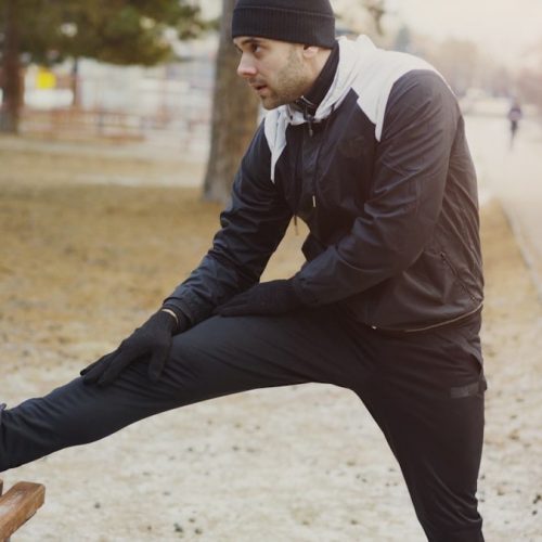 Young man runner doing stretching exercise preparing for morning workout and jogging in winter park